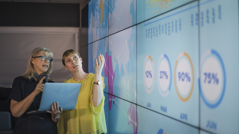 Businesswomen Discussing Ideas Against an Information Wall