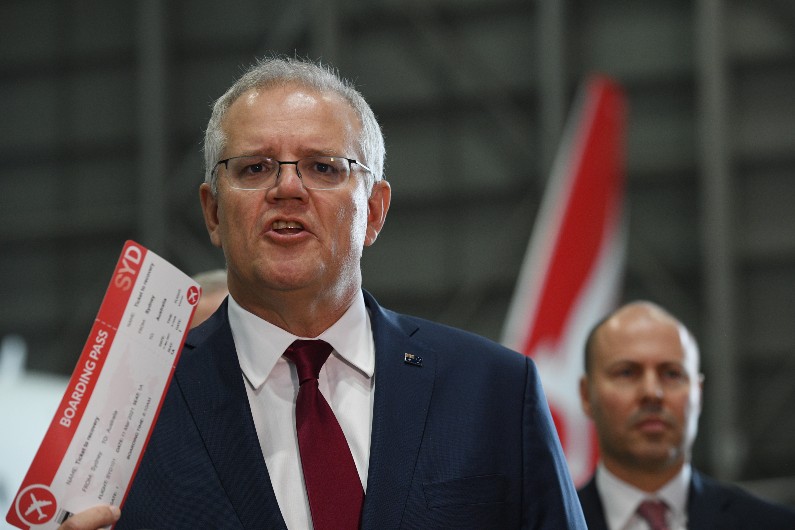 Scott Morrison holds up a novelty boarding pass titled 'Ticket to Recovery' at Sydney Airport