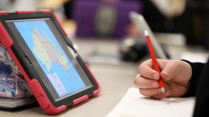 High school student using an electronic device or tablet style computer for reserach learning knowledge or reserach. Theme of classroom teaching teacher pedagogy educate and digital eductation with modern contemporary information technology IT for students and educators.